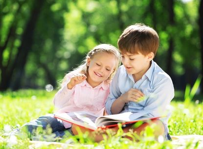 girl and boy reading a book in the park