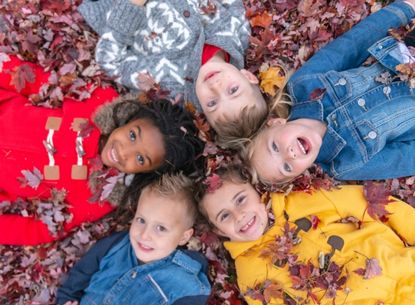 five kids with heads together lying in leaves
