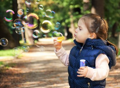 girl in blue vest blowing bubbles